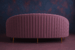 Curved plum velvet sofa with ribbed backrest, gold legs, and accent cushion in a modern purple-toned interior.