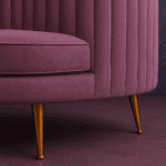 Curved plum velvet sofa with ribbed backrest, gold legs, and accent cushion in a modern purple-toned interior.