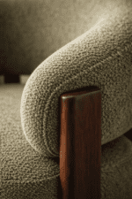 Close-up detail of sage green boucle fabric texture and dark walnut wood leg joint on a modern armchair